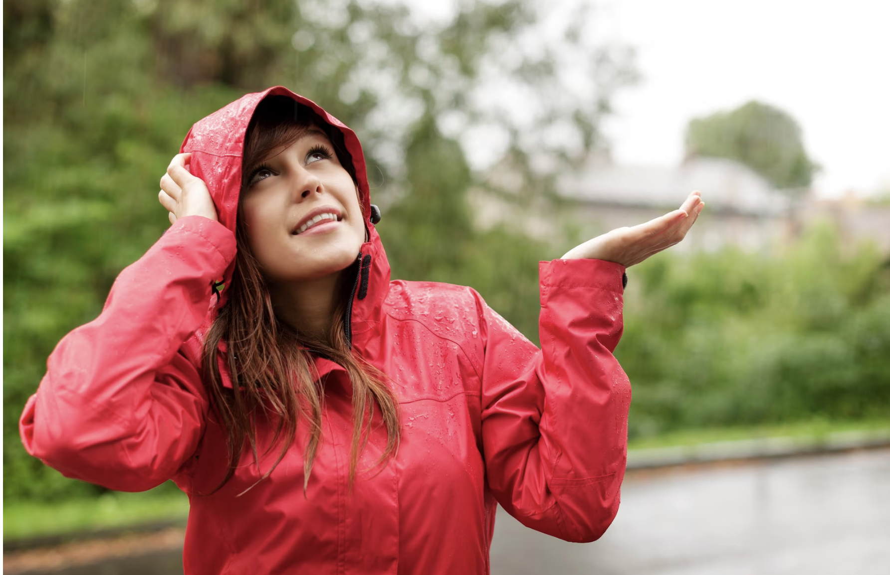 A woman in a red raincoat stands in the rain.