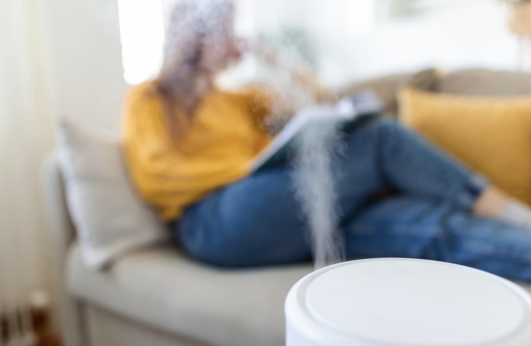A woman sits on the couch next to a humidifier.