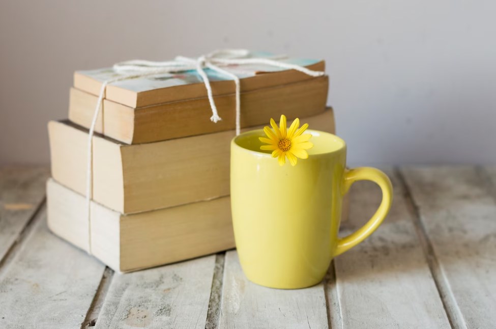 a yellow cup with a flower of the same color next to a pile of books