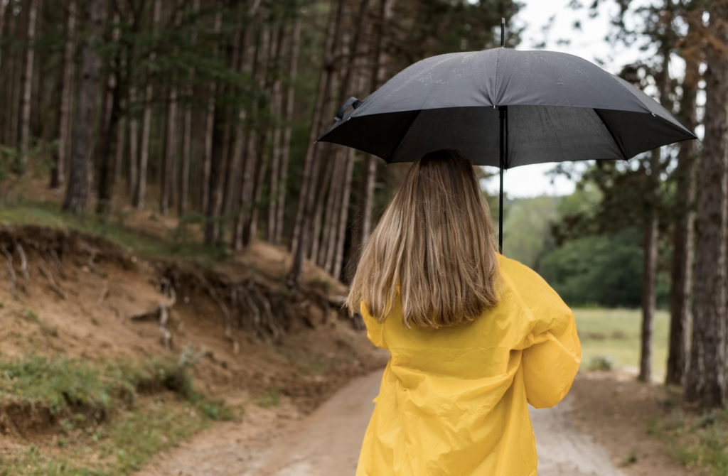 A girl walks under an umbrella in the woods during bad weather.