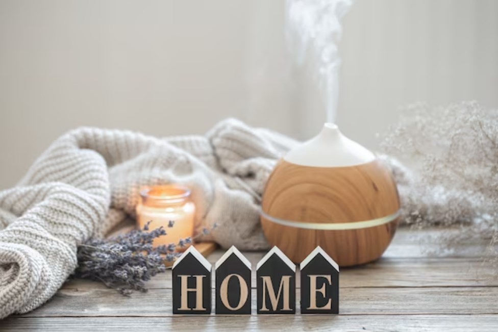 a modern aroma oil diffuser on a wooden surface with a knitted element, cozy details around, and the decorative word home